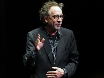 Tim Burton is wearing a black suit and a spec.